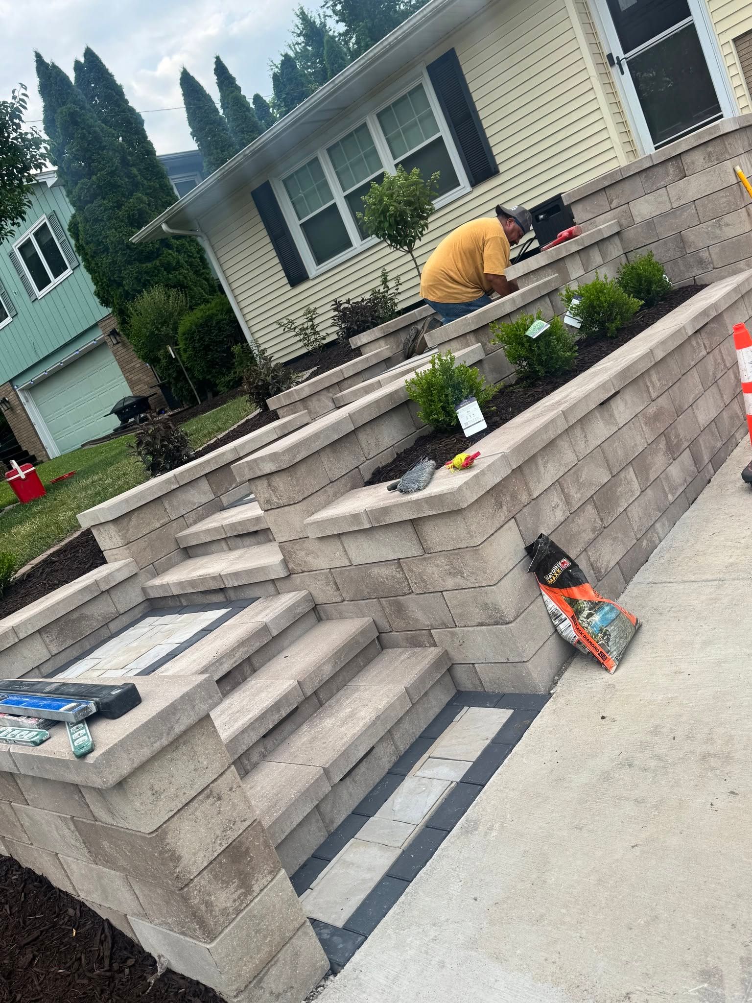 Worker crouching on front steps of a house, near a retaining wall and potted flowers.