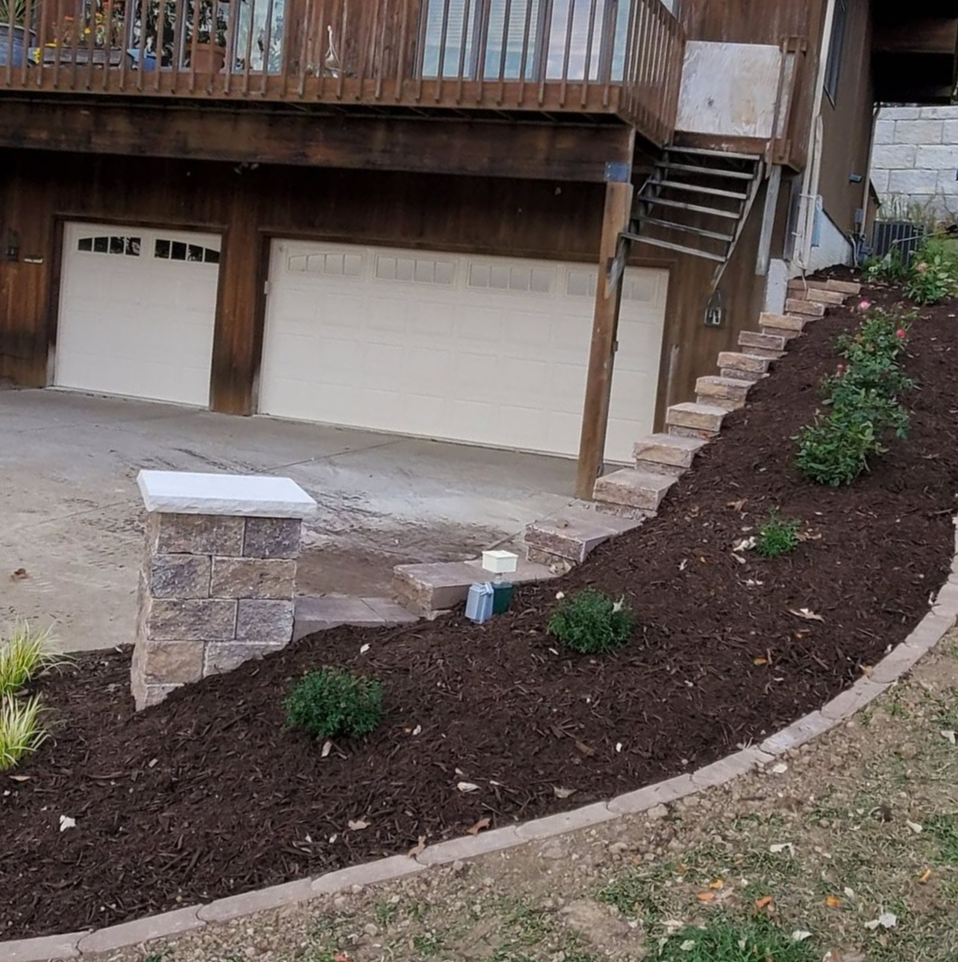 Curved mulch garden bed beside a slanted sidewalk outside a brick building with white doors and windows