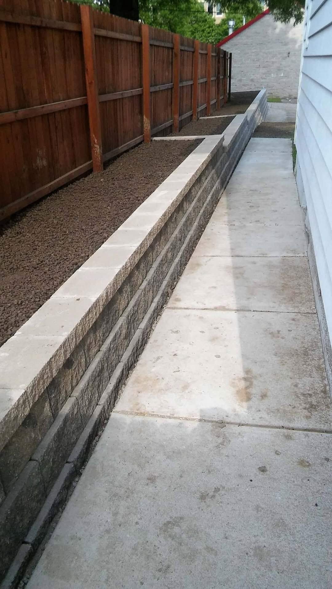 Concrete walkway with a long narrow channel beside a wooden fence and retaining wall