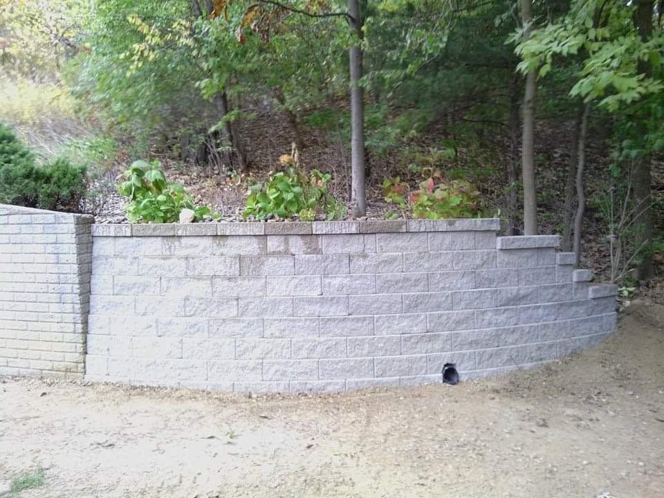 Curved gray stone retaining wall with flower bed and trees beside a dirt path