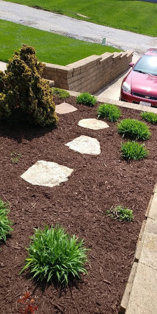 Landscaped front yard with stepping stones, shrubs, mulch, and a parked pink car by the curb