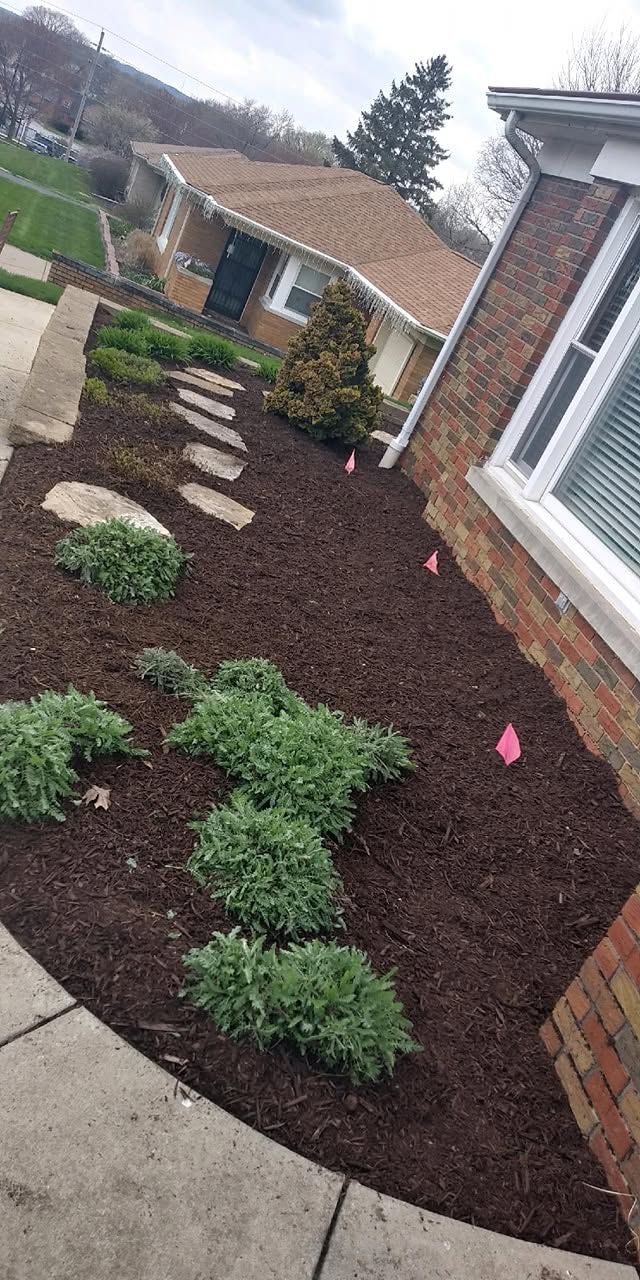 Slanted front yard with dark mulch, small shrubs, stepping stones, and brick house exterior.