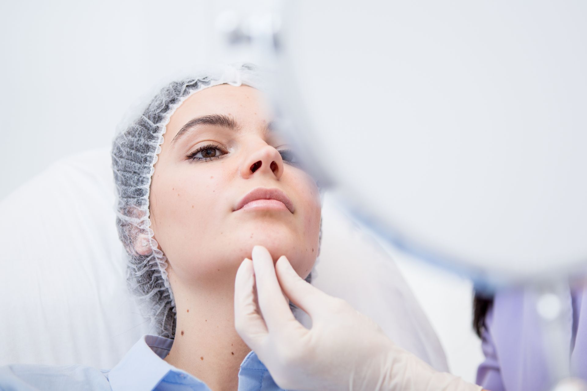 Donna in un ambiente medico con una mano guantata che esamina il volto di una paziente.