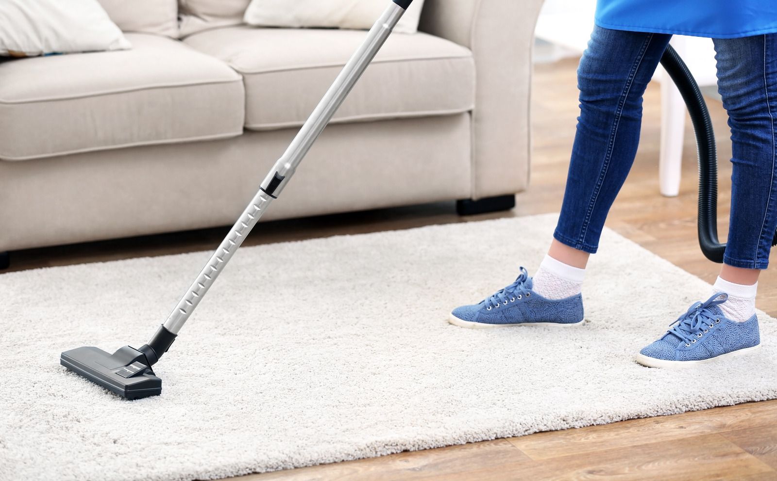A woman is using a vacuum cleaner to clean a rug in a living room.