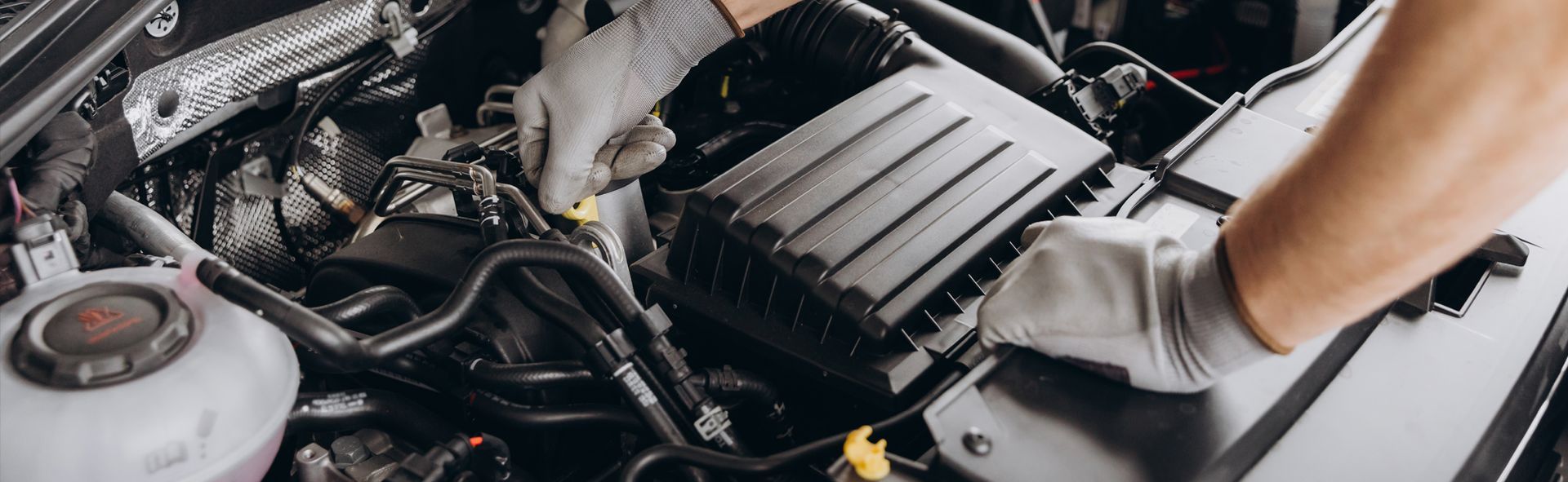 A mechanic wearing gloves works on a car engine.