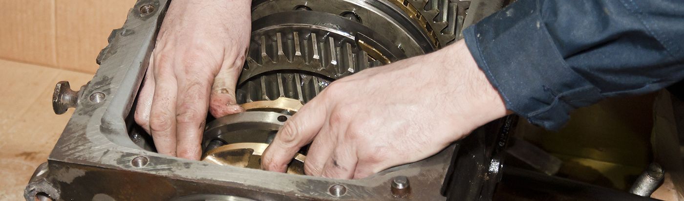 Close-up of hands working on the internal components of a disassembled mechanical transmission housing.