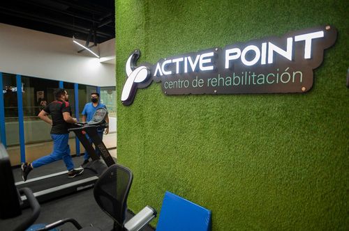 Una persona en una cinta de correr en el centro de rehabilitación Active Point. Un cartel en una pared verde.