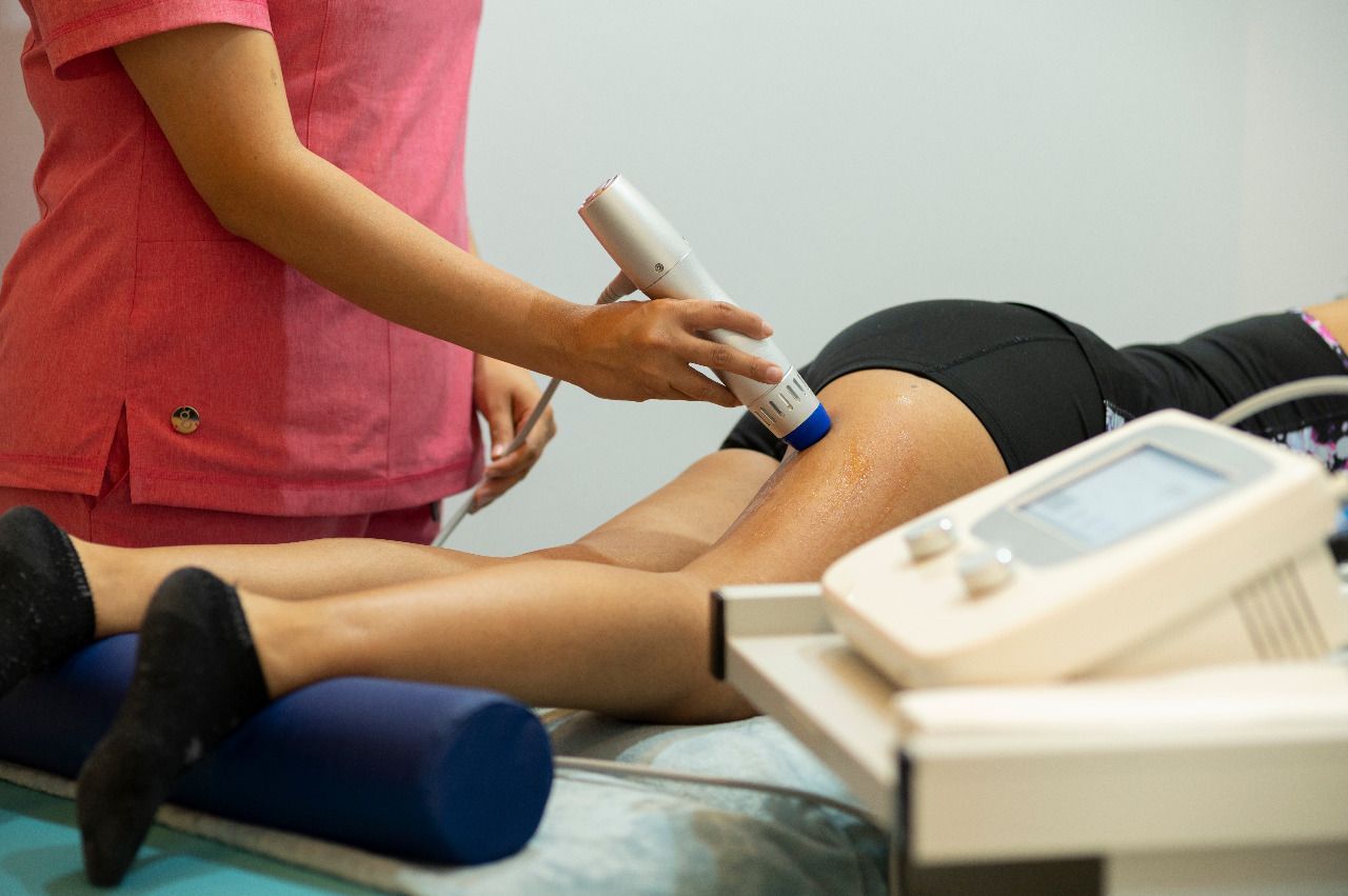 Terapeuta administra tratamiento de ultrasonido a la pierna del paciente en una mesa.