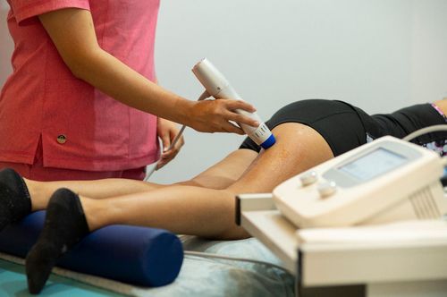 Persona recibiendo terapia de piernas con un dispositivo. Un terapeuta con camisa rosa aplica el tratamiento.