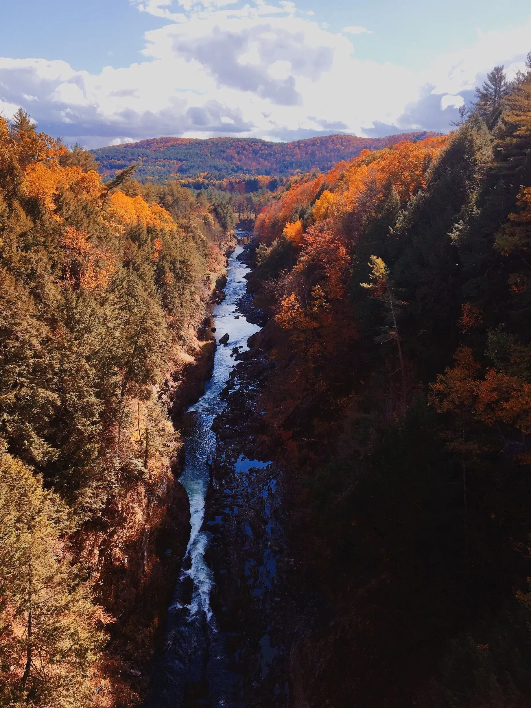 Autumn canyon with a waterfall flowing through colorful forested cliffs under a partly cloudy sky