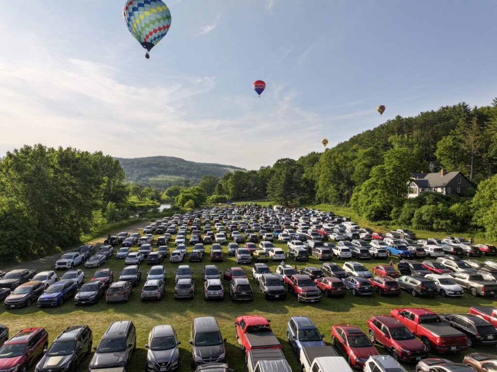 Parking lot full of cars at a countryside hot air balloon festival under a blue sky