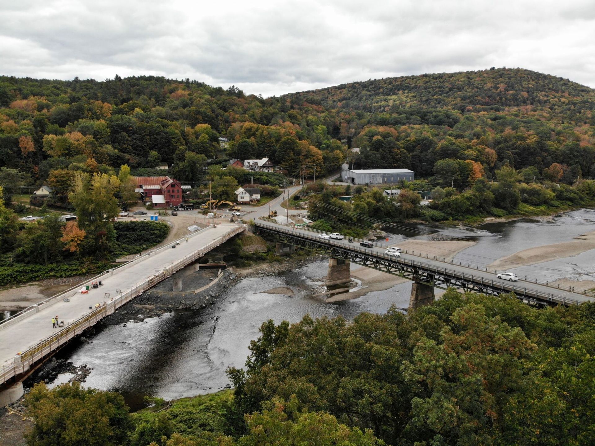 Aerial view of a bridge over a river beside a small town and wooded hills in autumn