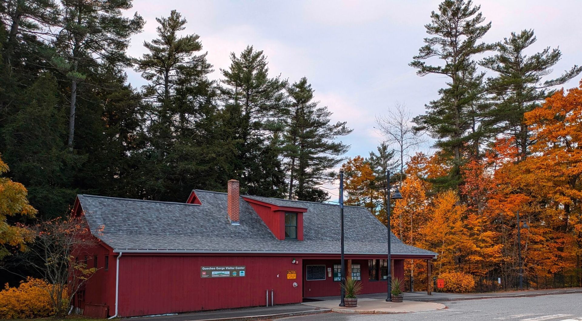 Red lodge-style building with gray roof among tall trees in autumn