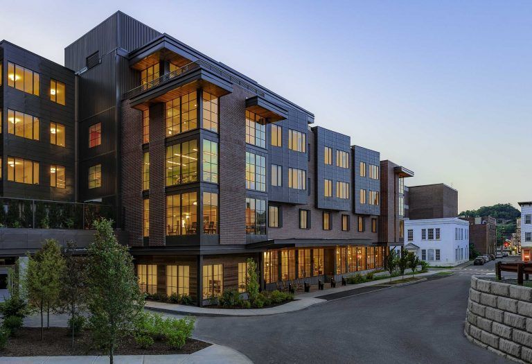 Modern multi-story building with lit windows at dusk on a quiet street.
