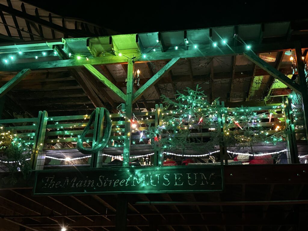 Illuminated outdoor display with green and white lights, wooden beams, and a sign reading “The Museum”