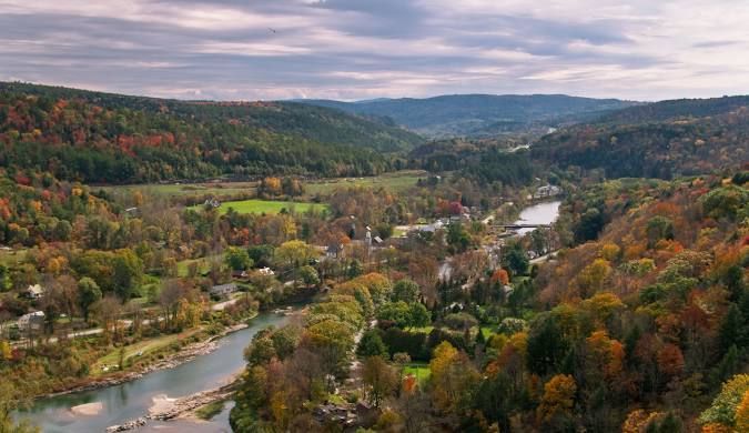 Aerial view of a river winding through a colorful autumn forested valley with hills in the distance