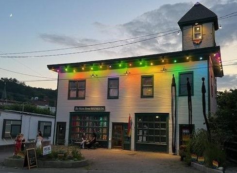 Colorful lights on a small white building with a tower at dusk, set against a cloudy sky
