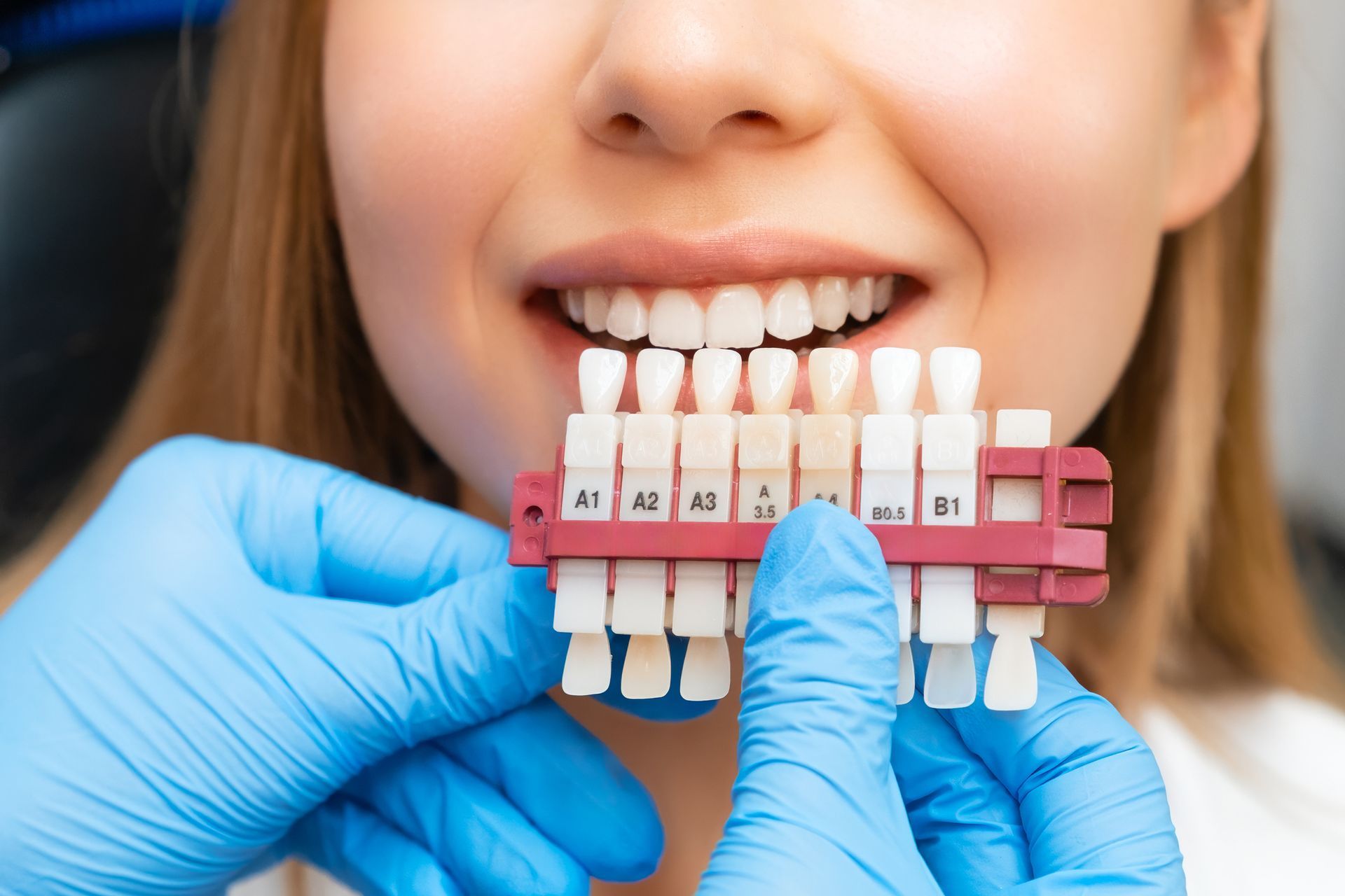 A woman is sitting in a dental chair looking at her teeth in a mirror.