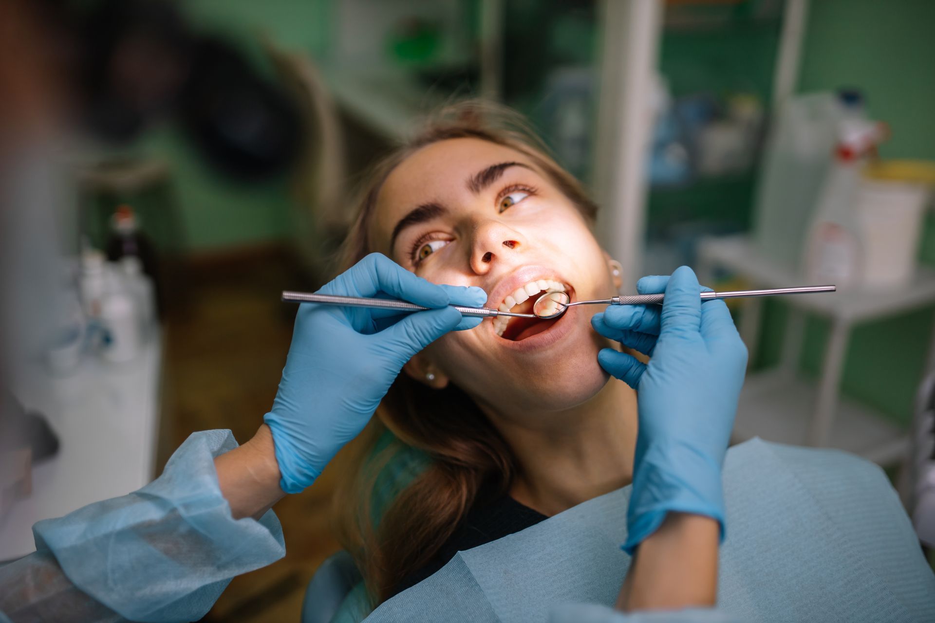 A woman is sitting in a dental chair while a dentist examines her teeth.