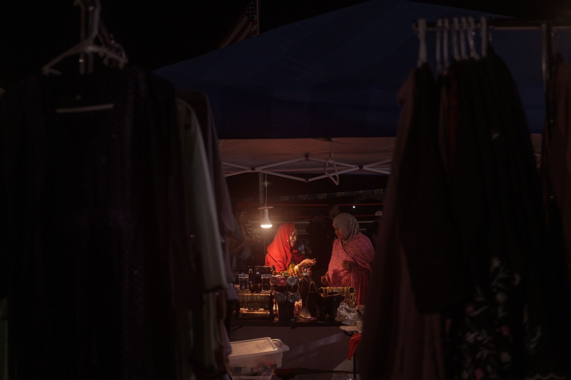 Two women examine goods for sale at a nightime street market. 