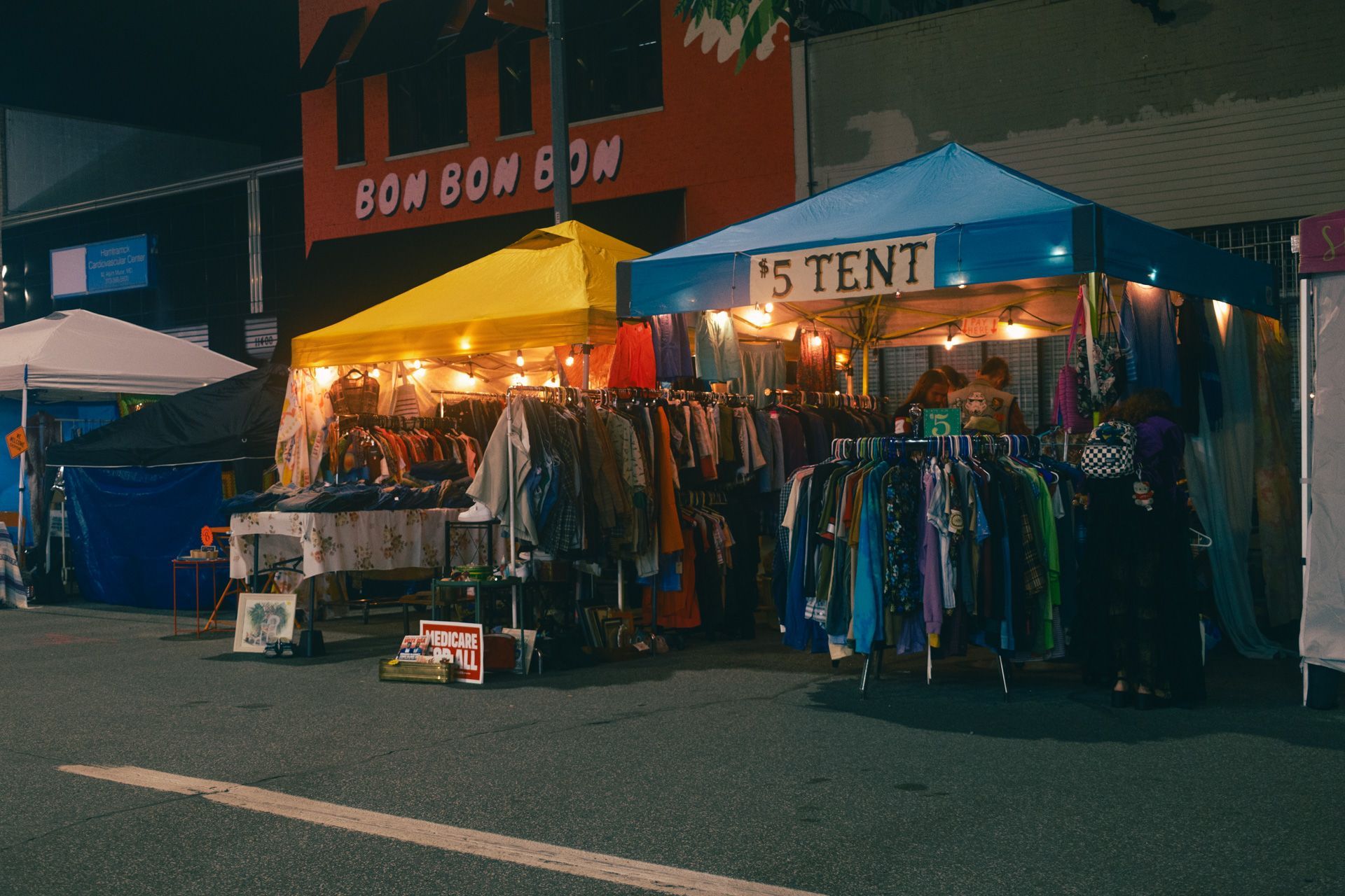 Brightly colored and illuminated tents filled with clothing for sale light up a nighttime street market in Detroit.