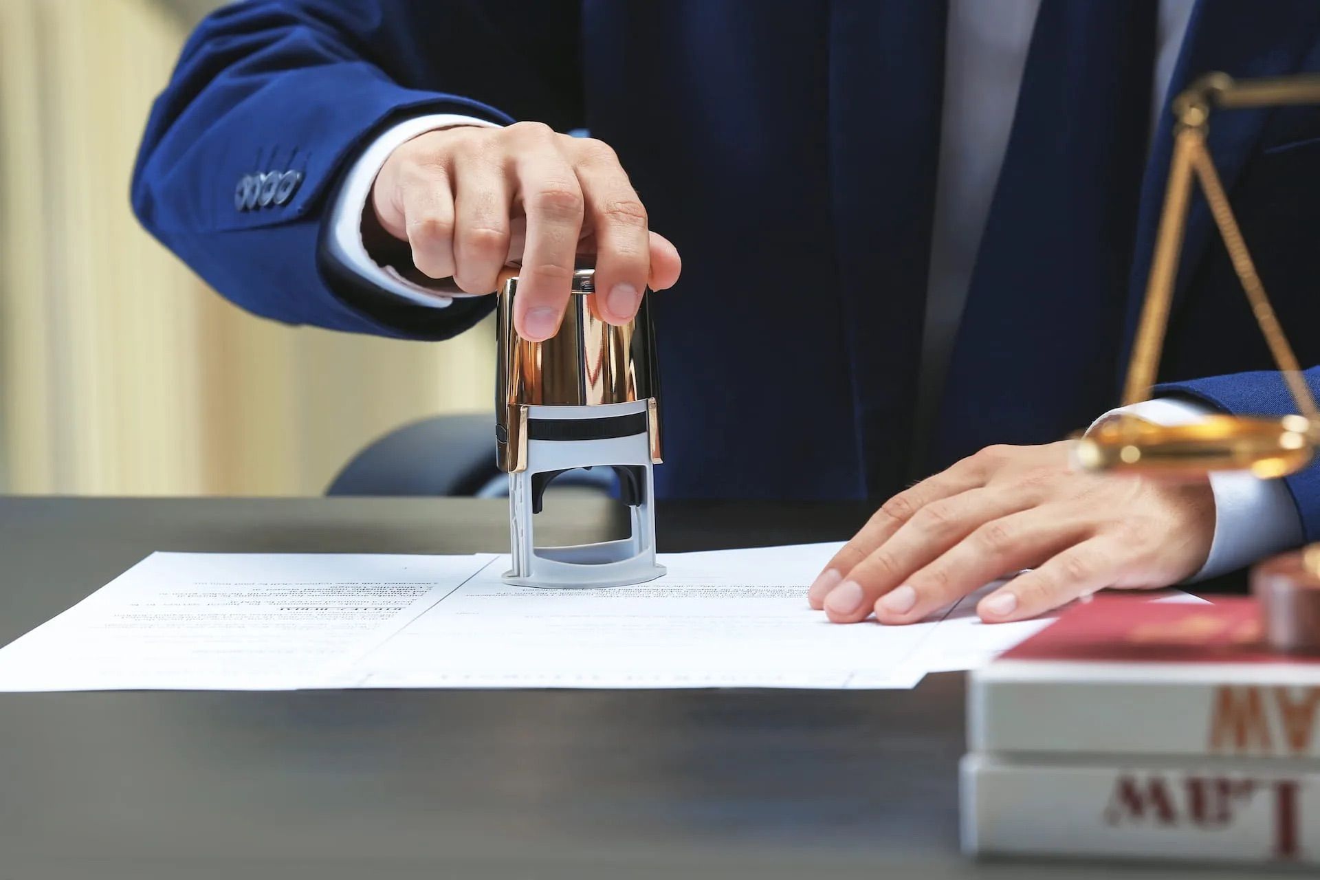Une personne en costume appose un tampon sur un document à un bureau, avec des ouvrages juridiques et une balance en arrière-plan.