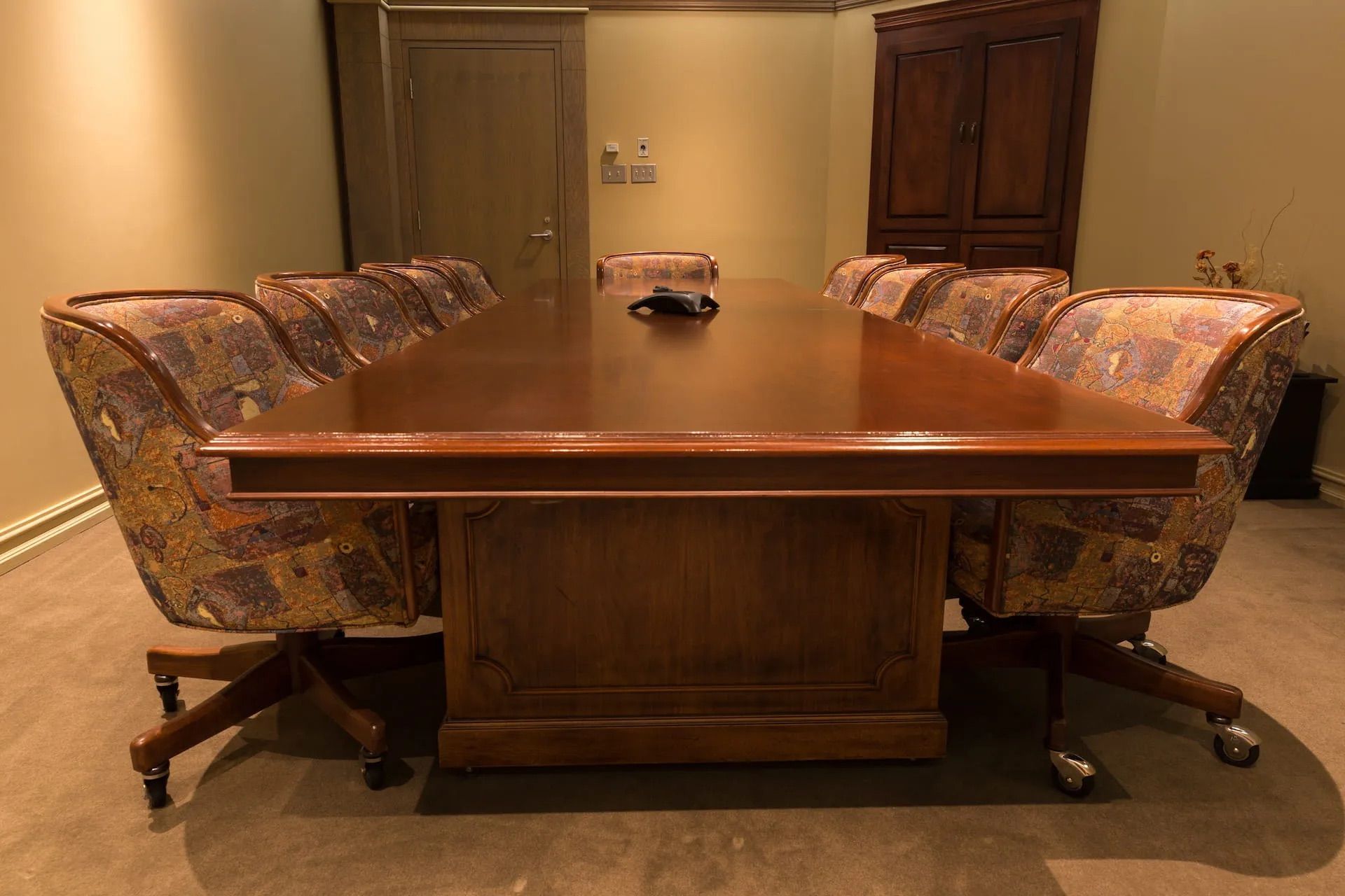 Salle de conférence avec grande table en bois, chaises à motifs et une armoire.