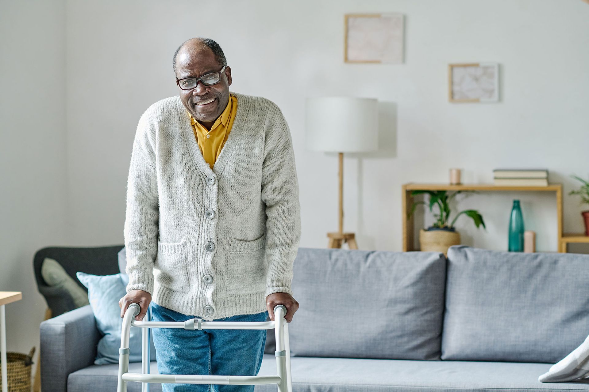 An elderly man is using a walker in a living room.