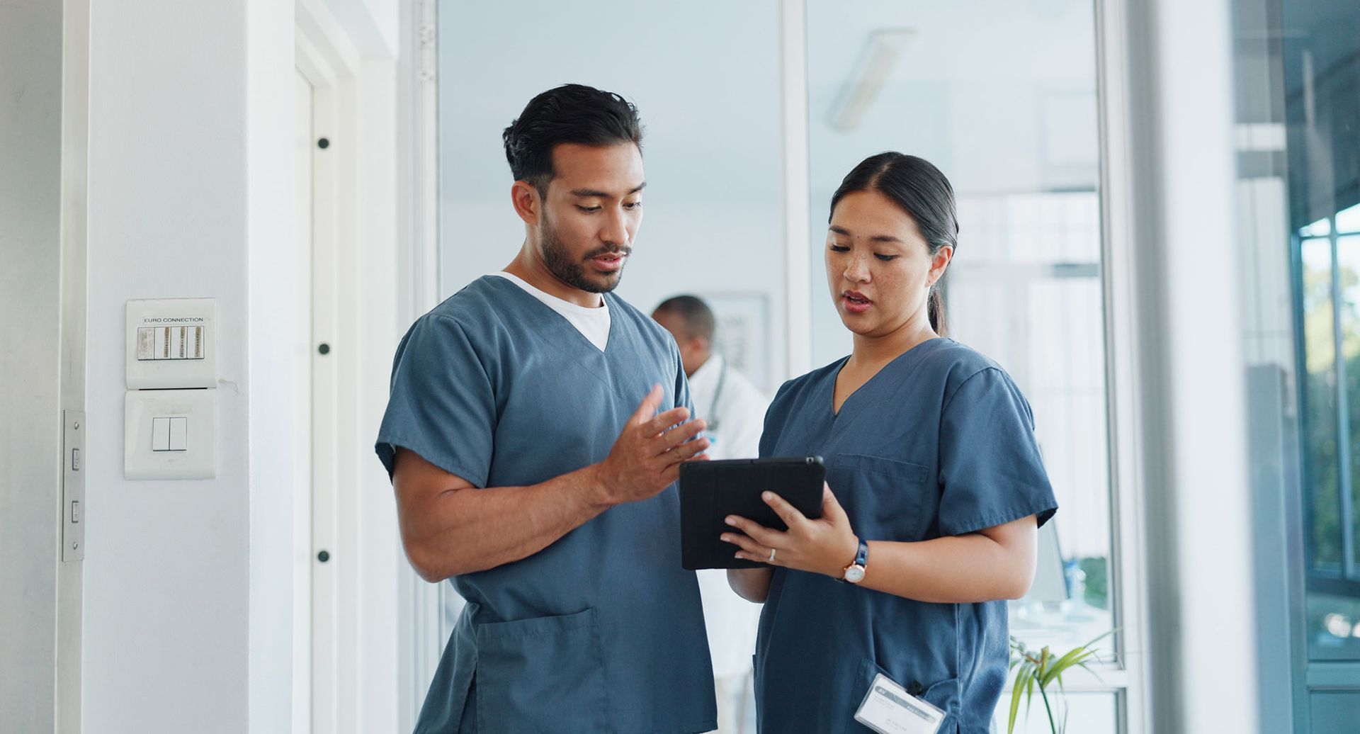 A man and a woman in scrubs are looking at a tablet.