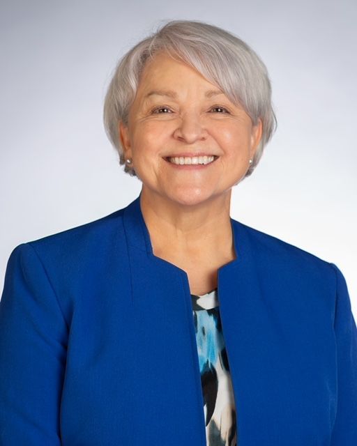 A woman is wearing a blue jacket and smiling for the camera.