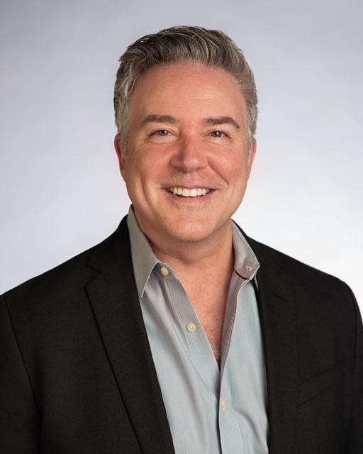 A man in a suit and blue shirt is smiling for the camera.