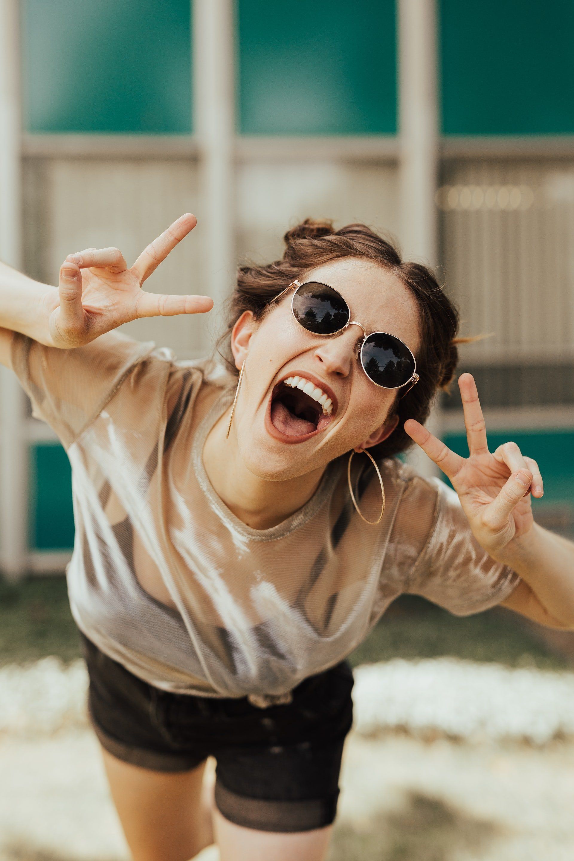 A woman wearing sunglasses is making a peace sign with her mouth open.