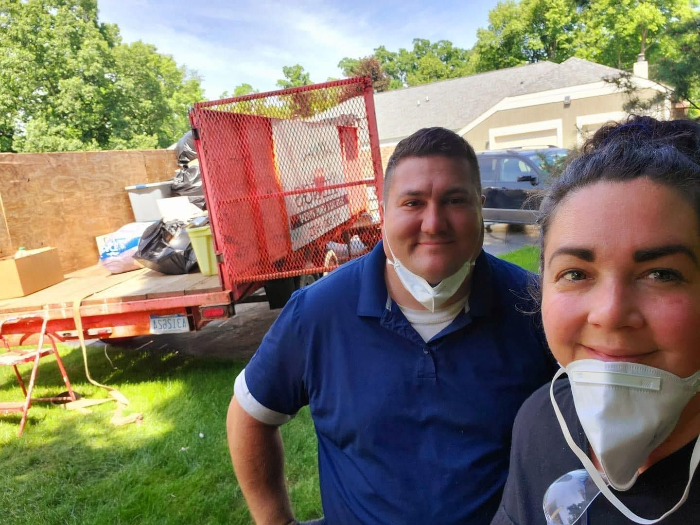 Two people outdoors beside a loaded truck and trailer in a sunny yard