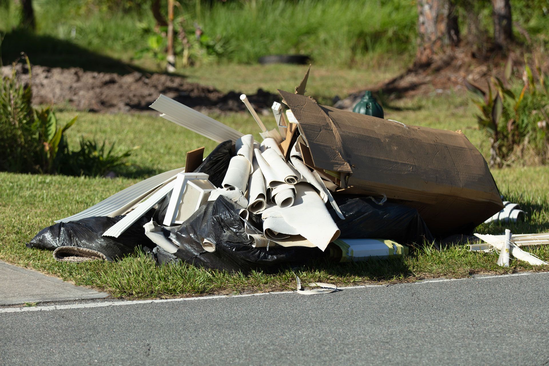 Pile of broken white and brown debris on a roadside near grass and pavement.
