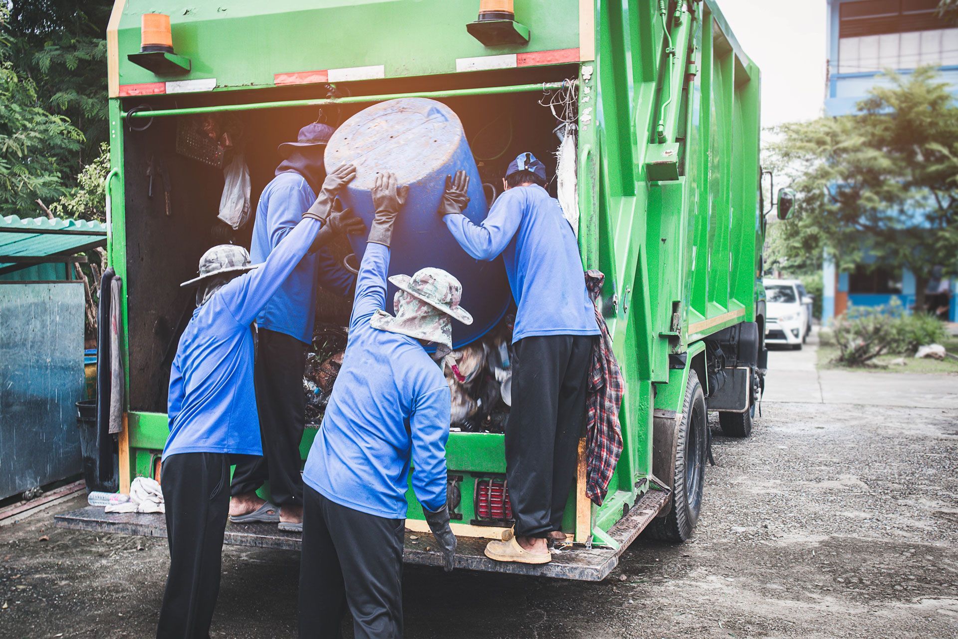 Workers in blue uniforms loading trash into a green garbage truck