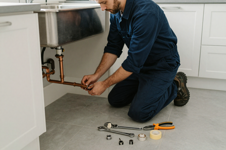 Plumber under kitchen sink replacing pipes