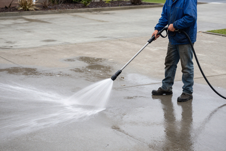Worker pressure washing concrete driveway