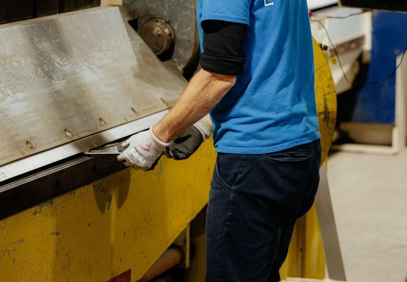 Personne utilisant une machine à cintrer les métaux portant des gants, dans une usine.