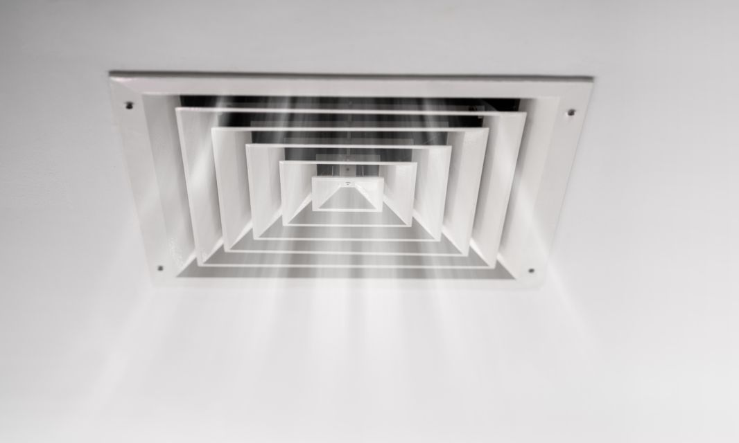 Grille d'aération blanche au plafond, d'où sort de l'air.