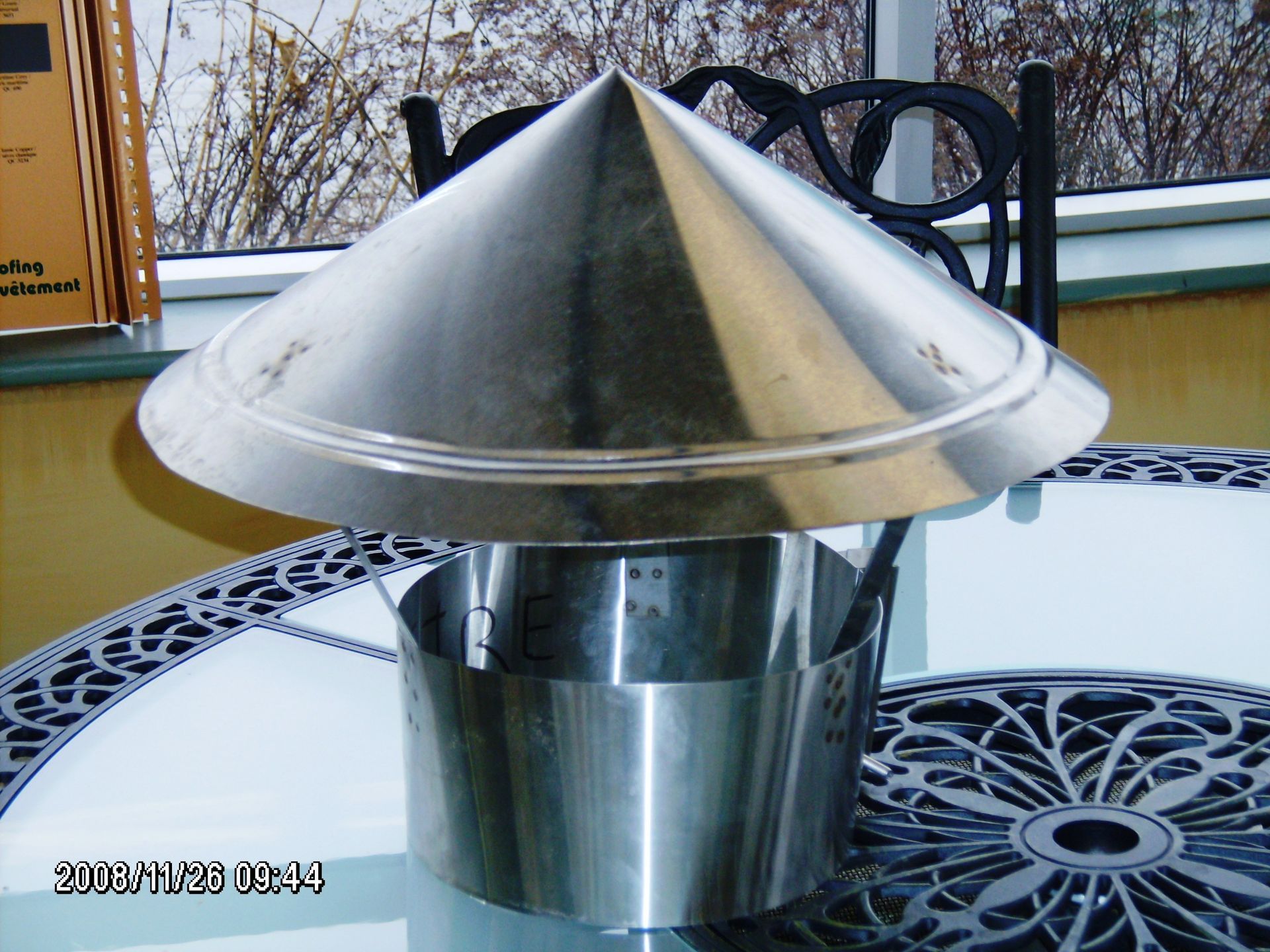 Un chapeau de cheminée en acier inoxydable se trouve sur une table devant une fenêtre