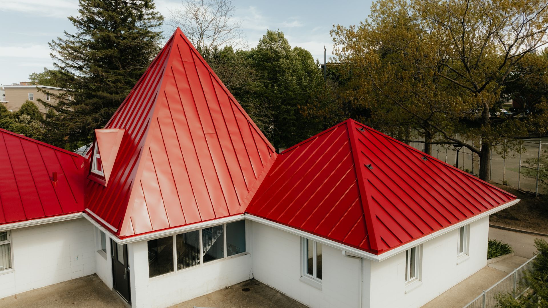Bâtiment blanc avec des toits rouges en angle, des arbres verts en arrière-plan.