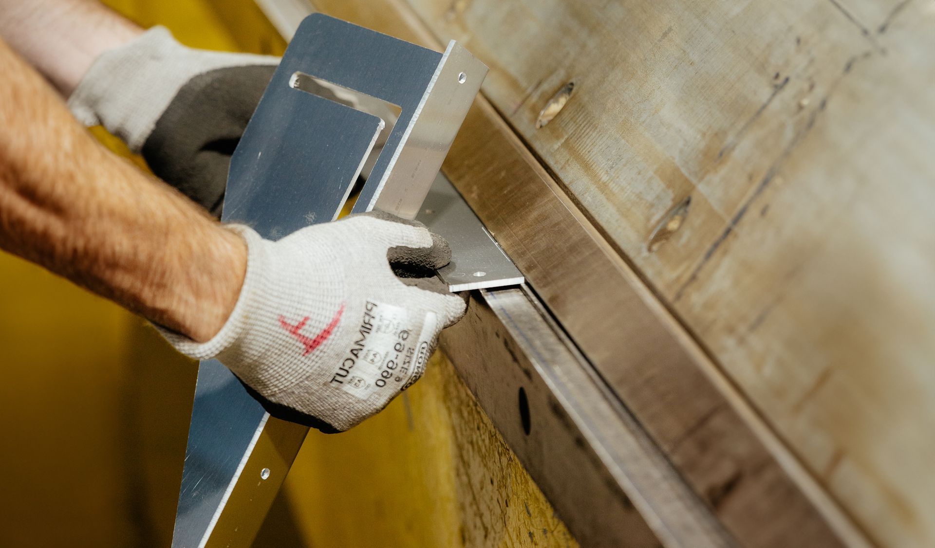 Une personne portant des gants, utilisant un outil carré en métal pour mesurer un morceau de métal.