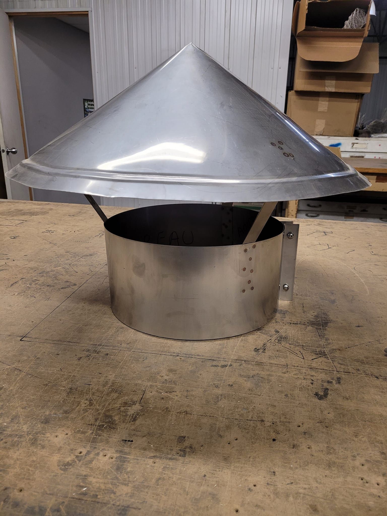 Un chapeau de cheminée en acier inoxydable est posé sur une table en bois.