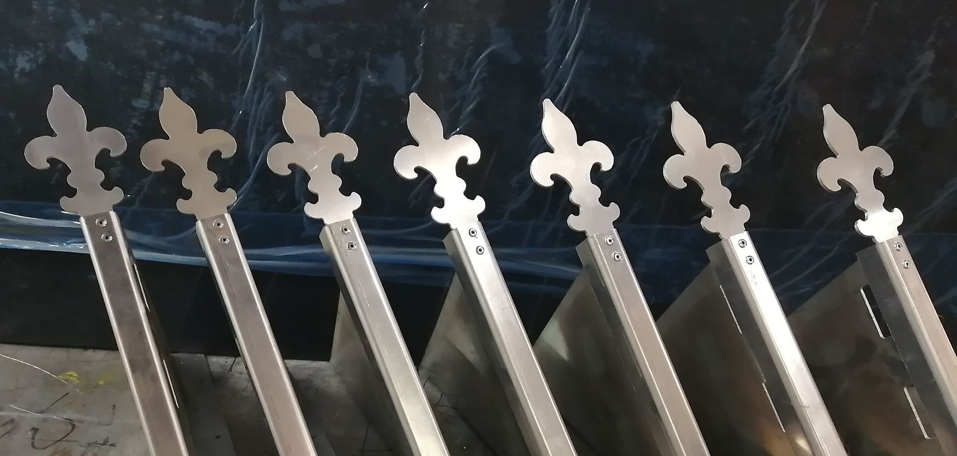 Ornements métalliques en forme de fleur de lys fixés aux panneaux de la clôture, probablement à des fins décoratives.