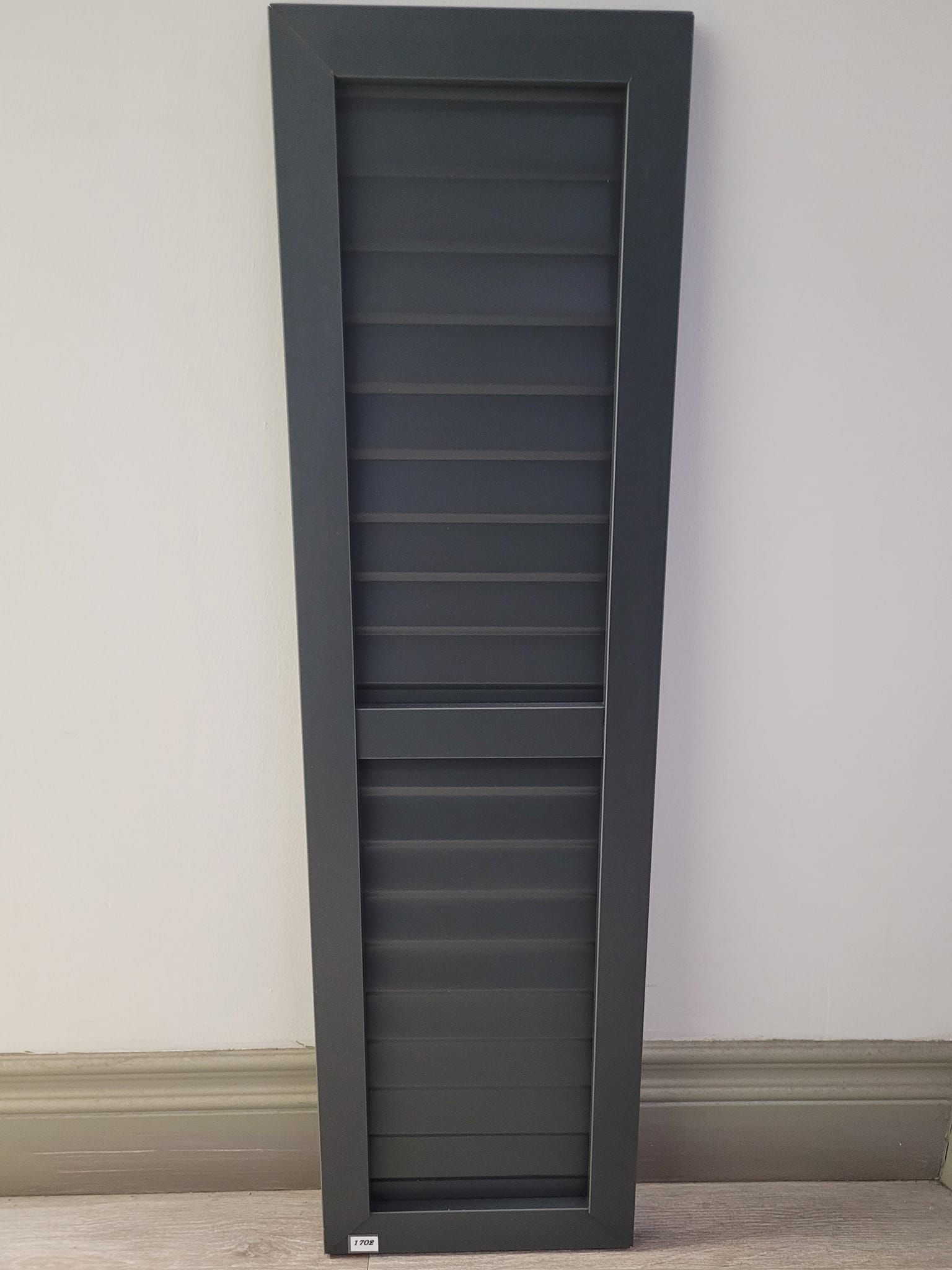Un volet noir est posé sur le sol à côté d'un mur.