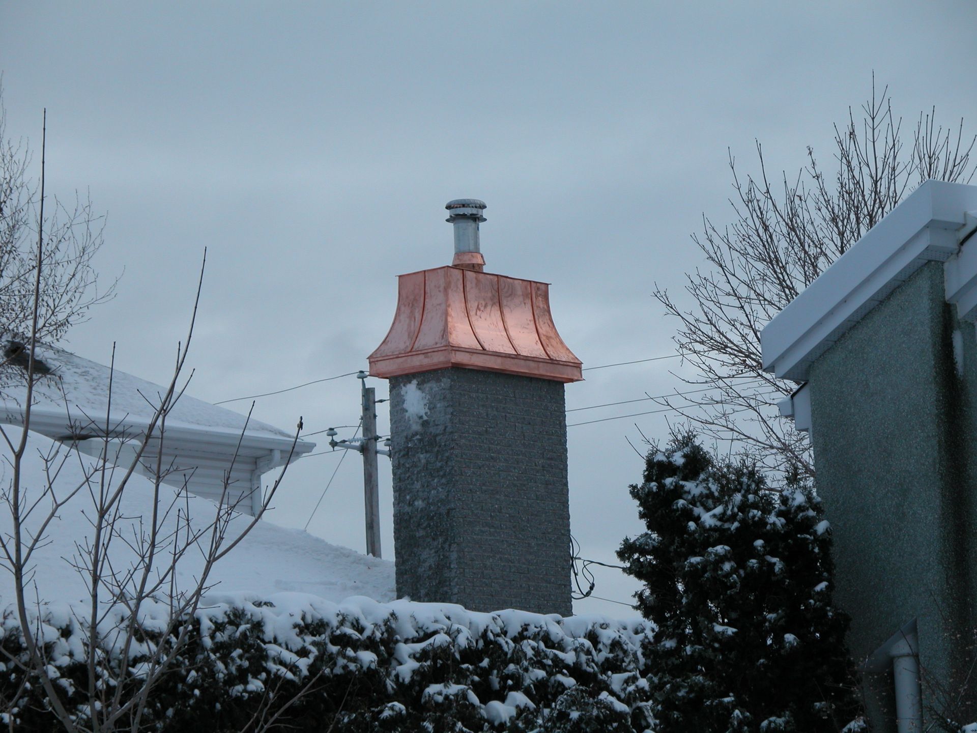 Une cheminée avec un toit en cuivre est entourée de neige