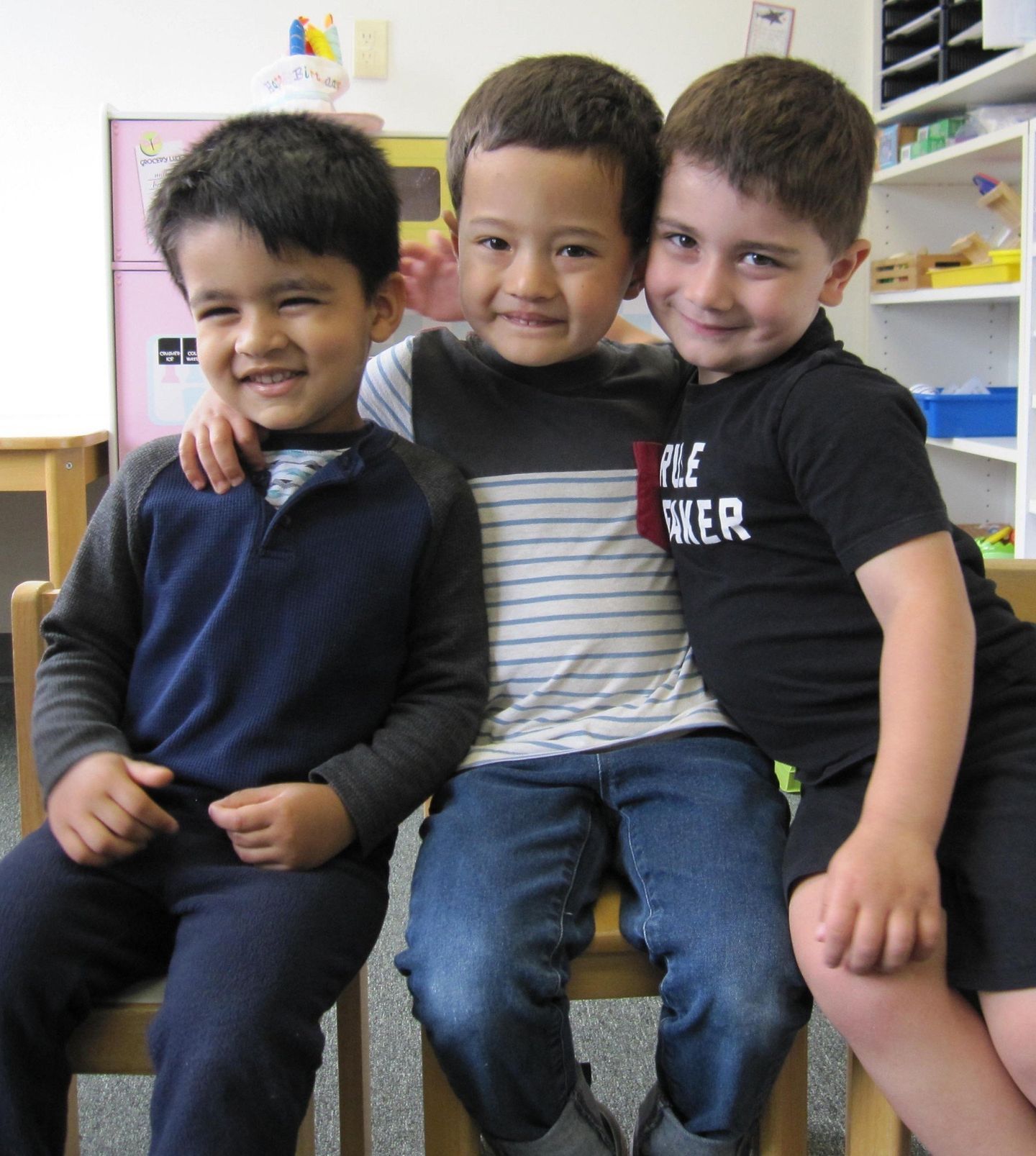 Three young boys, diverse skin tones, smiling and hugging, indoors