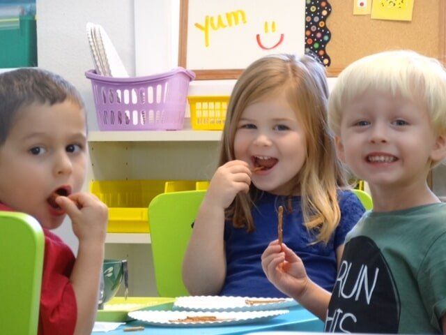 Three children at a table eating snacks, smiling