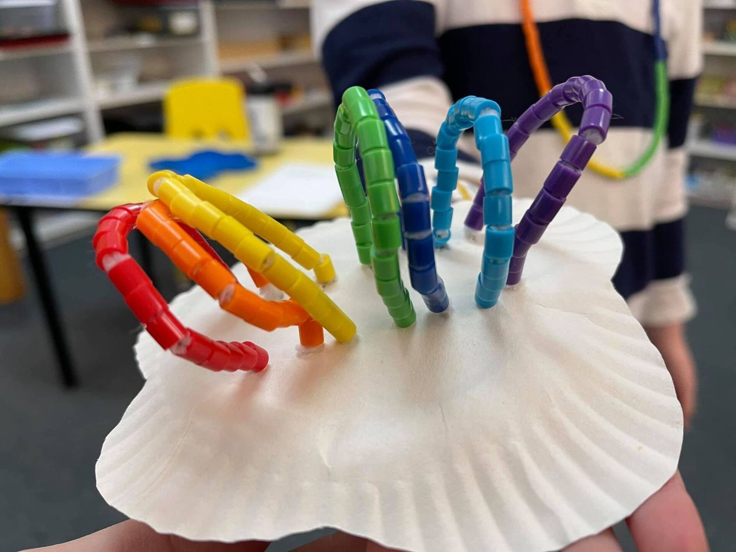 Rainbow-colored beads looped on a white seashell held by a person