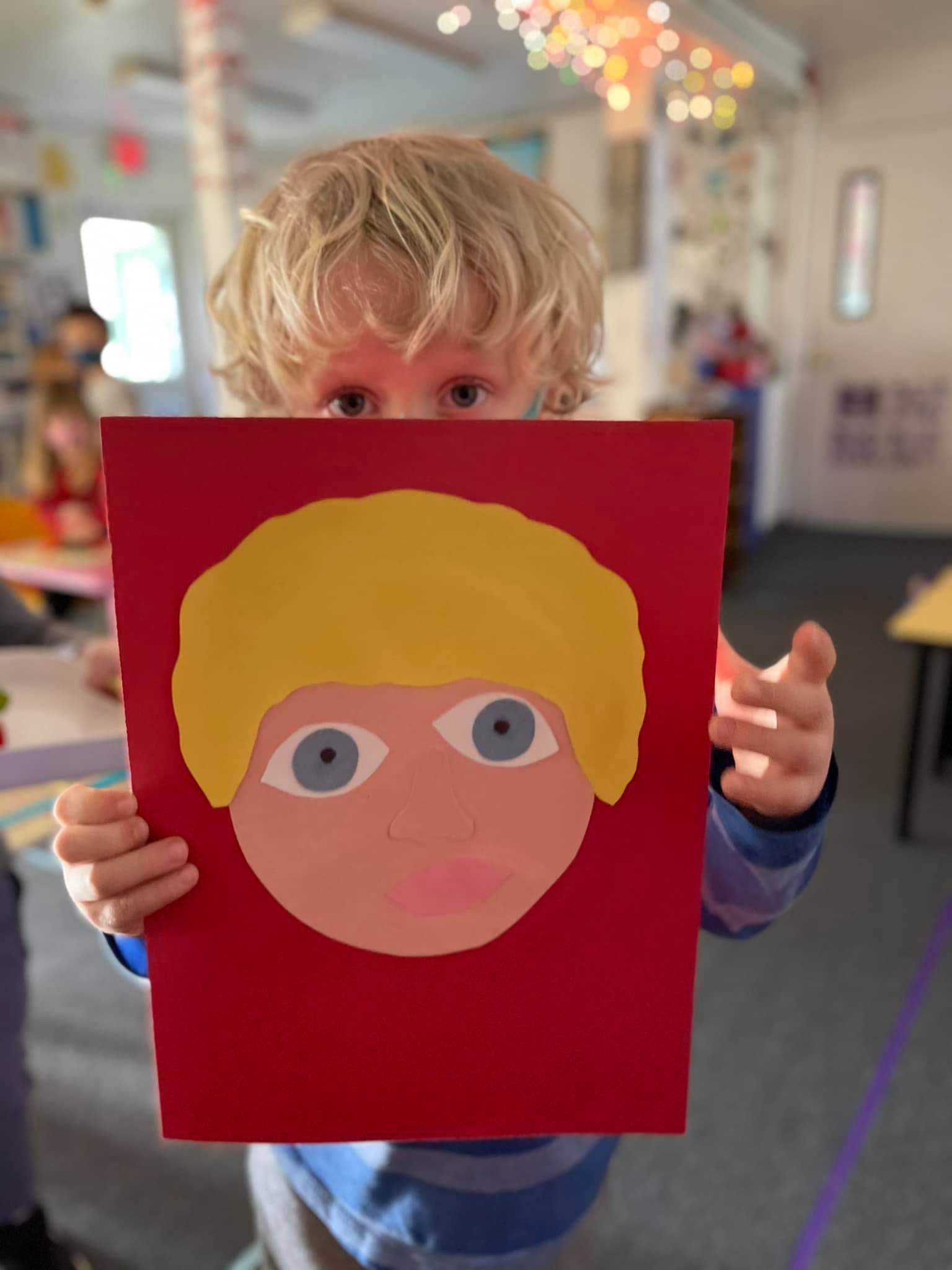 Young child holding a red paper with a painted face